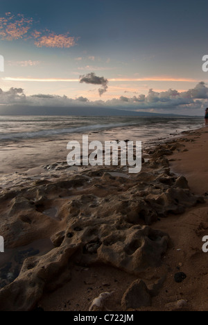 Tramonto su una bella spiaggia di Maui con le nuvole in lontananza e onde che lambiscono sui coralli sulla spiaggia Foto Stock