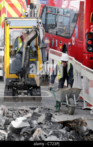 Lavoratori con vista aerea e miniescavatore che lavorano su lavori stradali nella corsia degli autobus accanto al traffico di rosso doppio pianista Autobus Regent Street West End Londra UK Foto Stock