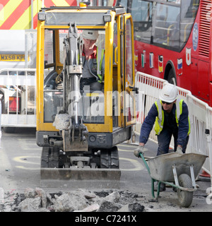 Lavoratori con vista aerea e miniescavatore che lavorano su lavori stradali nella corsia degli autobus accanto al traffico di rosso doppio pianista Autobus Regent Street West End Londra UK Foto Stock