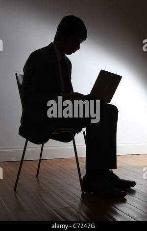 Silhouette di un giovane maschio indossa una tuta, seduta utilizzando un computer portatile. Foto Stock