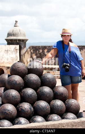 Un giovane di Puerto Rican donna turistica ponendo accanto al mucchio di sfere di canon a El Morro fortificazione nella vecchia San Juan. Foto Stock