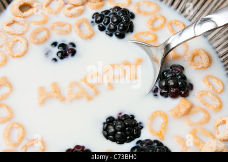 Le parole felice enunciato alla lettera a forma di pezzi di cereali galleggianti in un latte riempito ciotola di cereale. Foto Stock