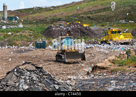 Bulldozer che lavorano in discarica e gabbiani con bruciatore a gas metano in background. Foto Stock
