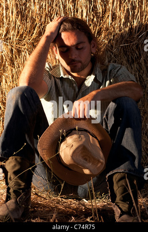 Stanco agricoltore Holding Hat seduto a terra Foto Stock