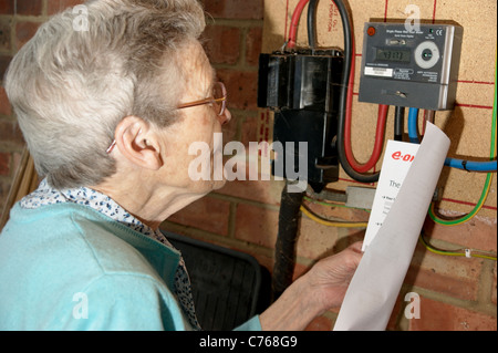 Donna anziana cerca & controllo elettricità e gas bollette con il misuratore in caso di discordanze Foto Stock