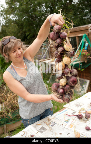 Una donna giardiniere con una stringa di cipolle che ella è cresciuta sul suo riparto garden, REGNO UNITO Foto Stock