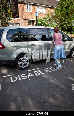 Donna con la gamba rotta di sblocco porta auto parcheggiate nel parcheggio disabili bay. Foto Stock