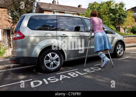 Donna con la gamba rotta di sblocco porta auto parcheggiate nel parcheggio disabili bay. Foto Stock