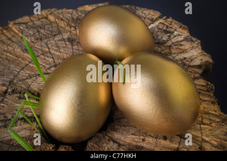 Tre uova d'oro su un blocco di trinciatura con erbacce emergenti Foto Stock