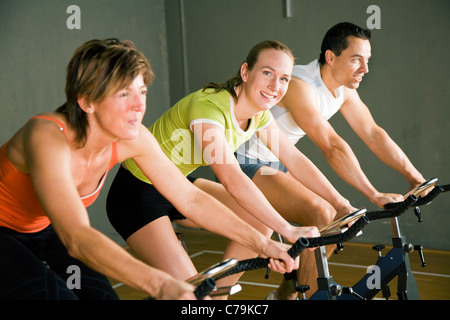 Tre persone in bicicletta in una palestra o fitness club, vestito in abiti colorati; concentrarsi sulla ragazza in mezzo Foto Stock