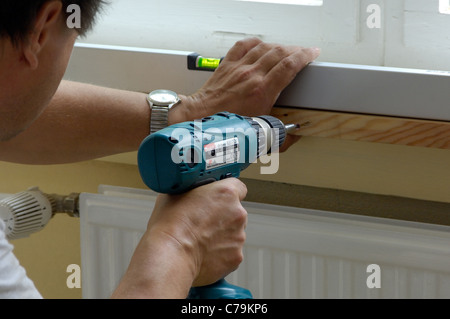 Workman avvitamento di un pannello di legno ad una parete Foto Stock