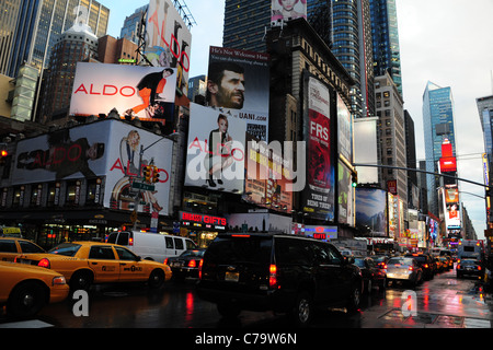 Traffico (vetture giallo taxi) in coda al neon rossa asfalto bagnato 7th Avenue anteriore inserzioni grattacielo verso Times Square di New York City Foto Stock