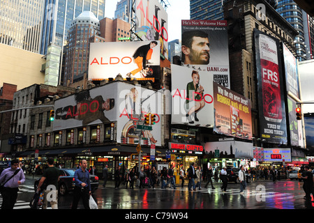 Molte persone che attraversano rosso neon blu asfalto bagnato 7th Avenue di fronte grattacielo inserzioni, angolo 48th Street, New York City, Stati Uniti d'America Foto Stock