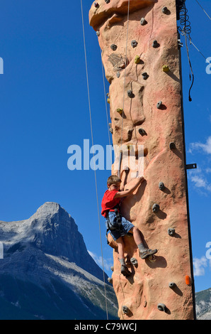 Ragazzino sulla parete di arrampicata con le montagne sullo sfondo, Canmore, Alberta, Canada Foto Stock
