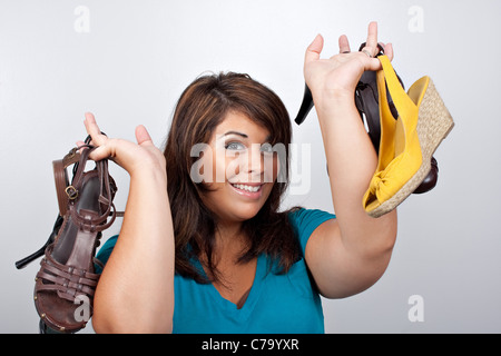 Una giovane donna che mantiene molte scarpe diverse su uno sfondo color argento. Foto Stock