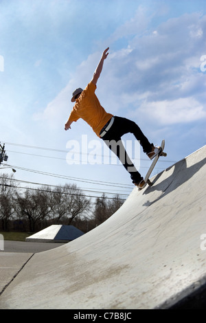 Ritratto di un giovane guidatore di skateboard pattinaggio giù una rampa di skate park. Foto Stock