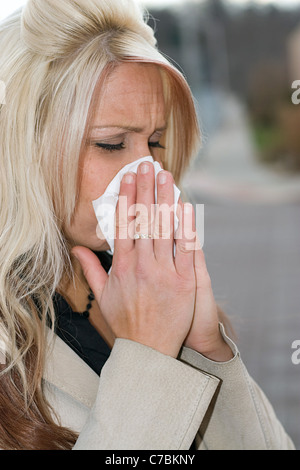Questa giovane donna di starnuti ripetuti in un tessuto o ha un raffreddore o veramente male le allergie. Foto Stock
