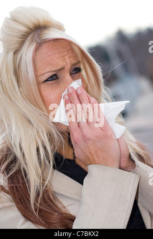 Questa giovane donna di starnuti ripetuti in un tessuto o ha un raffreddore o veramente male le allergie. Foto Stock