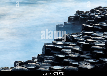 Spruzzi delle onde su colonne di basalto vicino al tramonto, Giant's Causeway, County Antrim, Irlanda del Nord, Regno Unito