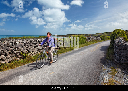 Donna Bicicletta Equitazione sul muro di pietra alberato sull isola di Inishmore, Isole Aran, nella contea di Galway, Repubblica di Irlanda Foto Stock