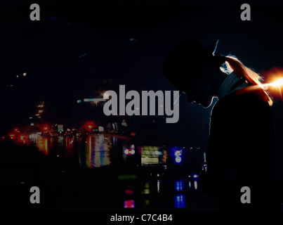 Silhouette di donna con cappello in piedi la città di notte con illuminazione Foto Stock
