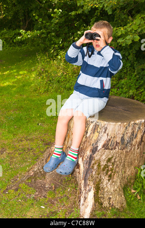 A sette anni di vecchio ragazzo birdwatching con il binocolo a Fairhaven bosco e acqua da giardino in Sud Walsham , Norfolk , Regno Unito Foto Stock