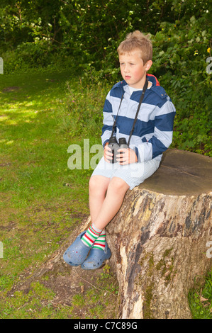 A sette anni di vecchio ragazzo birdwatching con il binocolo a Fairhaven bosco e acqua da giardino in Sud Walsham , Norfolk , Regno Unito Foto Stock