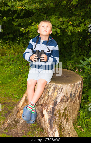 A sette anni di vecchio ragazzo birdwatching con il binocolo a Fairhaven bosco e acqua da giardino in Sud Walsham , Norfolk , Regno Unito Foto Stock