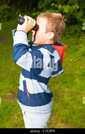 A sette anni di vecchio ragazzo birdwatching con il binocolo a Fairhaven bosco e acqua da giardino in Sud Walsham , Norfolk , Regno Unito Foto Stock