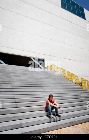 Un ragazzo che si siede sui gradini di ingresso alla Casa da Musica di Porto è l'ascolto di musica. Foto Stock