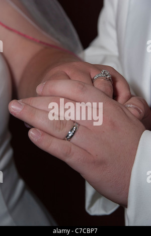 Coppia di sposi appena sposati che si tengono per mano e mostrano le loro bande nuziali ad alta risoluzione Foto Stock