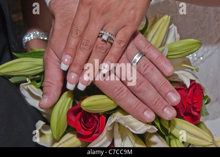 Giovane coppia interrazziale sposata di recente che si esibisce con le sue bande nuziali con bouquet nuziale in alta risoluzione sullo sfondo Foto Stock