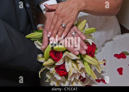 Giovane coppia interrazziale sposata di recente che si esibisce con le sue bande nuziali con bouquet nuziale in alta risoluzione sullo sfondo Foto Stock