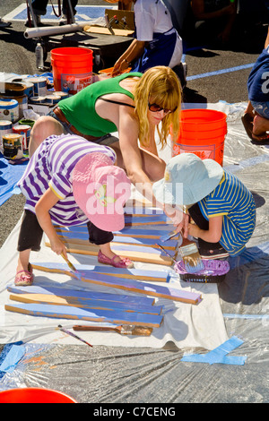 Una giovane donna di volontari e le figlie di lei le decorazioni di vernice su un edificio della città durante una comunità abbellimento programma. Foto Stock