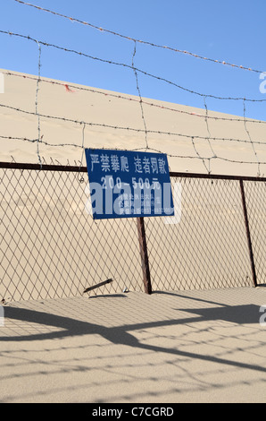 Un alto recinto che separa i visitatori tra le dune a Dunhuang, del Gansu in Cina. Il segno avverte di eventuali ammende per i trasgressori Foto Stock