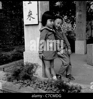 1950s. Foto storiche di due figli, un ragazzo e una ragazza appoggiata contro un pilastro con caratteri cinesi, a Macao. Foto Stock