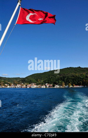 Bandiera turca e la piccola pesca e villaggio turistico di Anadolu Kavagi in background . Lo Stretto del Bosforo, Istanbul. Foto Stock