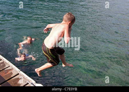 Ragazzo balza in lago dal dock, divertimento estivo famiglia Foto Stock