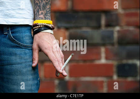 Tatuato adolescente tenendo un giunto di Cannabis Foto Stock