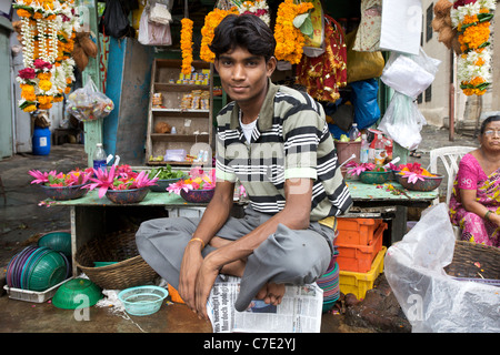 Ritratto di un giovane ragazzo asiatico seduto di fronte a un mercato in stallo, che vende offerte indù, in Mumbai, India Foto Stock