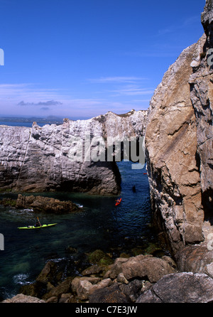 Sea kayakers passando sotto Bwa Gwyn mare naturale arco rock nelle scogliere vicino a Rhoscolyn Isola di Anglesey North Wales UK Foto Stock