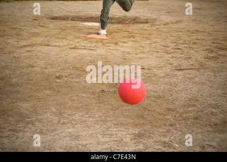 Un rosso kickball rotoli verso casa dopo la piastra è passo - la persona raffigurata qui sulla piastra si avvicina al calcio. Foto Stock