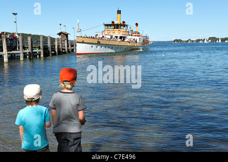 Bambini su foreshore guardando un Chiemsee Ferry Boat al Herreninsel, Chiemgau Alta Baviera Germania Foto Stock