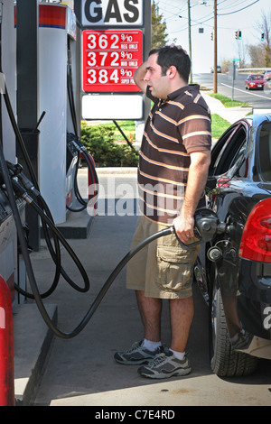 Un uomo di pompaggio a prezzo elevato del gas nella sua auto con un disgustato guarda sul suo volto. Foto Stock