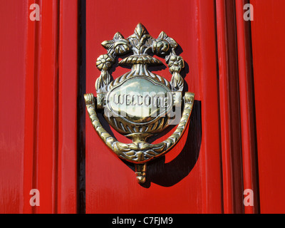 Un Benvenuto in ottone respingente su una porta rossa Foto Stock