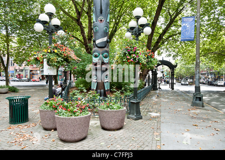 Lato ovest Pioneer Square riproduzione lampioni moderni Tlingit totem pole cesti floreali pendenti distante ghisa pergola arch Foto Stock