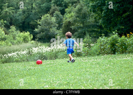 Giovane ragazzo americano afghano, a caccia di una sfera rossa giù per la collina nel cortile giardino, Missouri USA Foto Stock