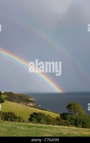 Un colorato arcobaleno doppio splendenti sul mare con scuri pioggia nuvole all'orizzonte. Foto Stock