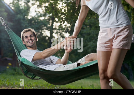 Un uomo disteso in una amaca tirando la sua ragazza verso il basso Foto Stock