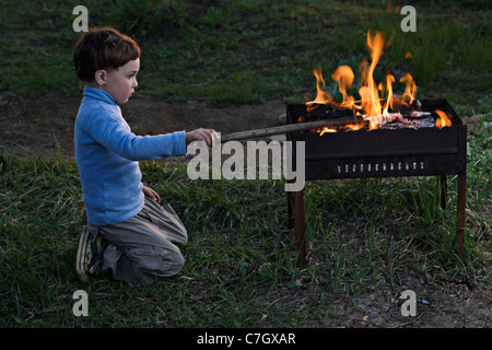 Un ragazzo prendendo in corrispondenza di un fuoco in un esterno di una buca per il fuoco Foto Stock